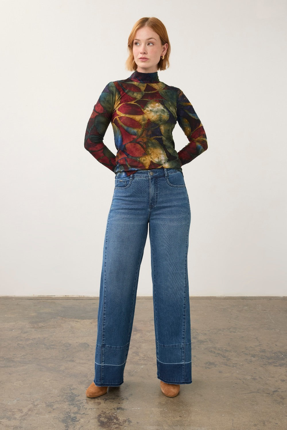 Broderick's Clothing Co. long sleeve mock neck top with a bold multi-colored abstract print worn with wide-leg jeans.