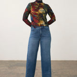 Broderick's Clothing Co. long sleeve mock neck top with a bold multi-colored abstract print worn with wide-leg jeans.