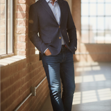 Broderick's Clothing Co. navy denim knit sport coat worn by a man leaning against a brick wall in a sunlit room.