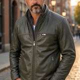 Broderick's Clothing Co. olive green leather bomber jacket with a stand-up collar worn by a man on a city street.