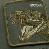 Broderick's Clothing Co. olive trucker hat featuring a detailed embroidered patch of a vicious snake head