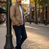 Broderick's Clothing Co. tan lamb leather jacket with stand-up collar worn by a man on a city street at sunset.