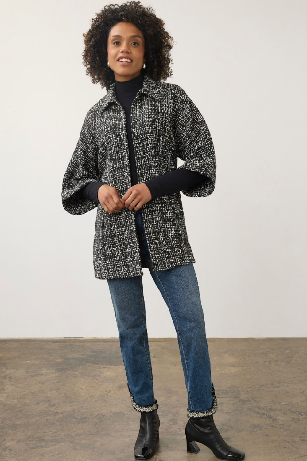 Model wearing a Broderick's Clothing Co. black and white tweed poncho jacket with wide sleeves over blue jeans.