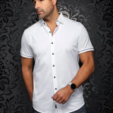 Man wearing a white shirt with black buttons against a dark patterned wall