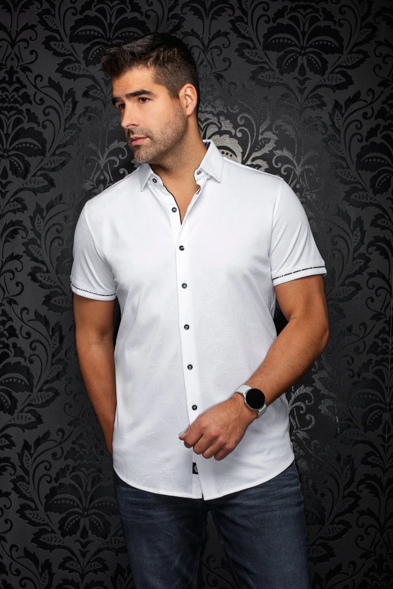 Man wearing a white shirt with black buttons against a dark patterned wall