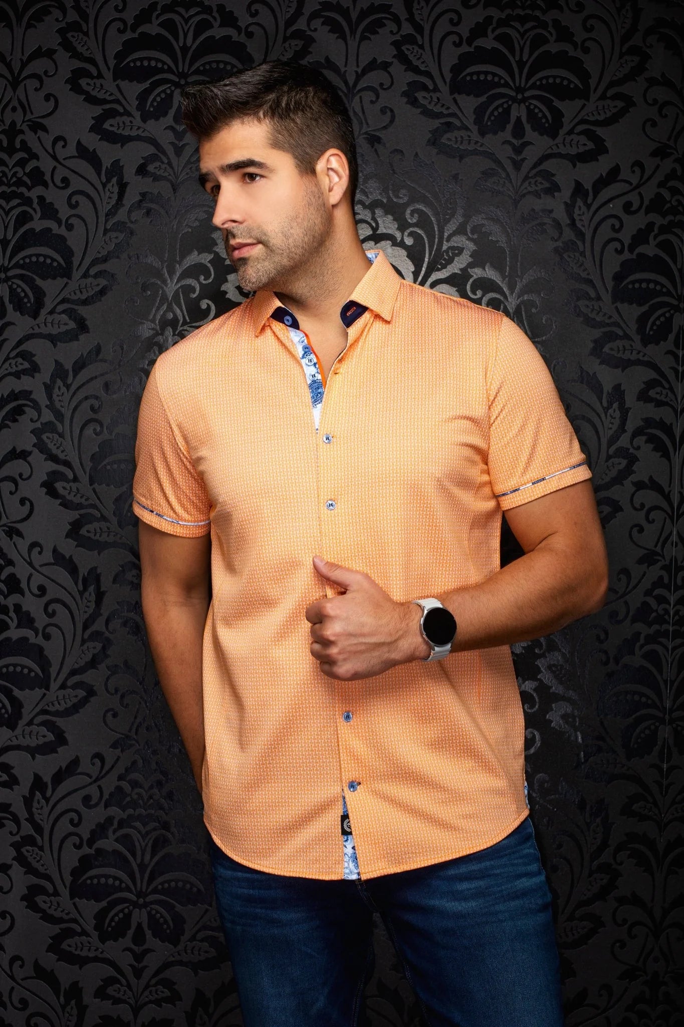 Man wearing an orange patterned shirt against a dark decorative background