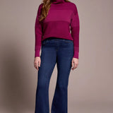 Woman wearing a magenta sweater and blue jeans against a beige background
