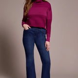 Woman wearing a purple sweater and blue jeans against a beige background
