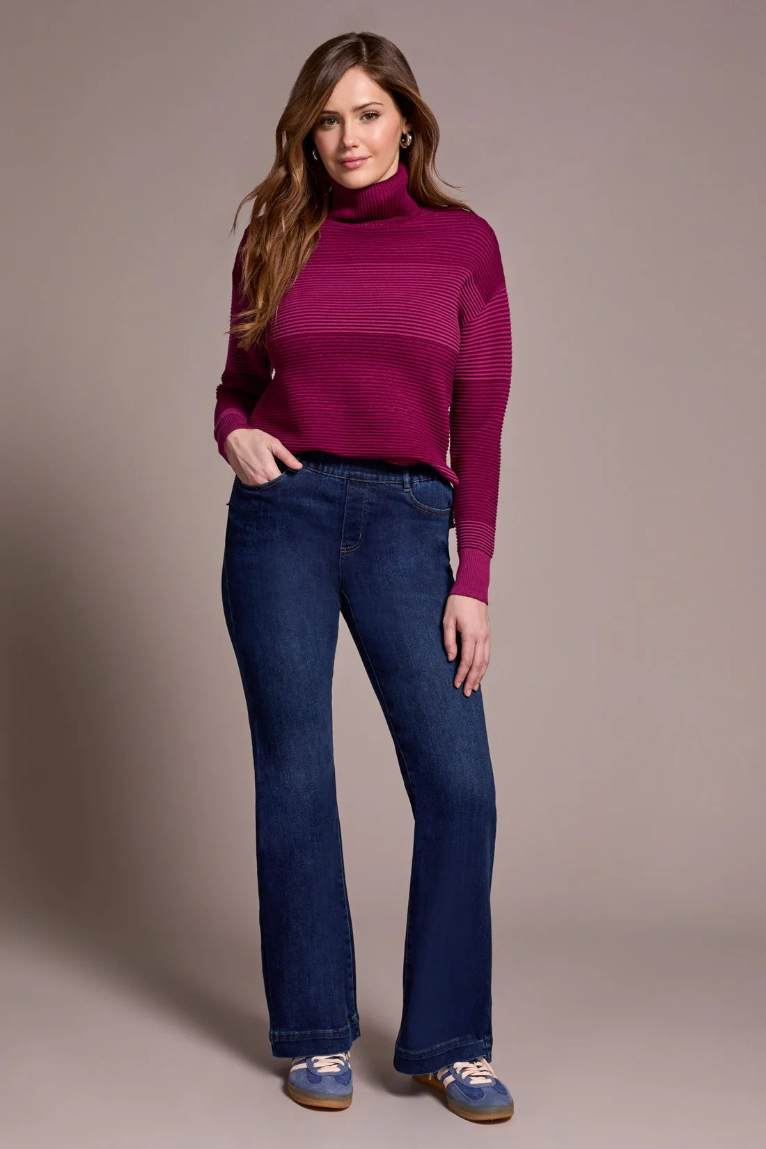 Woman wearing a purple sweater and blue jeans against a beige background