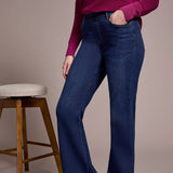 Person wearing a purple sweater and blue jeans standing next to a wooden stool against a beige background