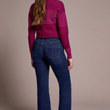Woman wearing a magenta sweater and blue jeans against a beige background