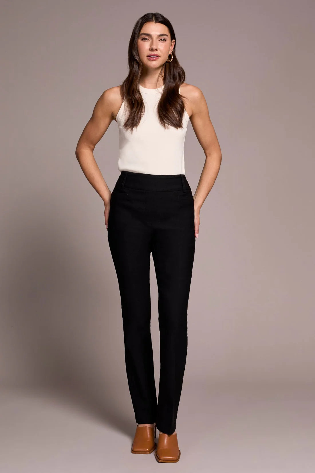 Woman wearing a white sleeveless top and black pants against a neutral background