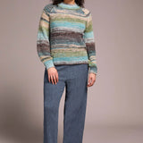Woman wearing a colorful striped sweater and blue pants against a plain background