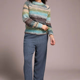 Woman wearing a colorful striped sweater and blue jeans against a plain background