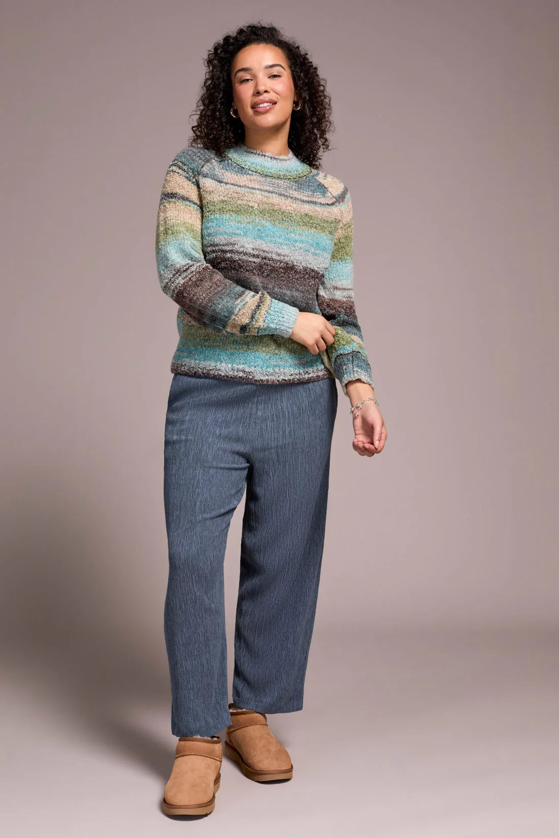 Woman wearing a colorful striped sweater and blue jeans against a plain background