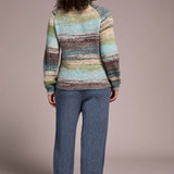 Person wearing a multicolored striped sweater and blue pants on a plain background