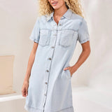 Woman wearing a light blue denim dress in a neutral setting
