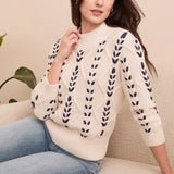 Woman wearing a cream sweater with black leaf patterns sitting on a beige couch.
