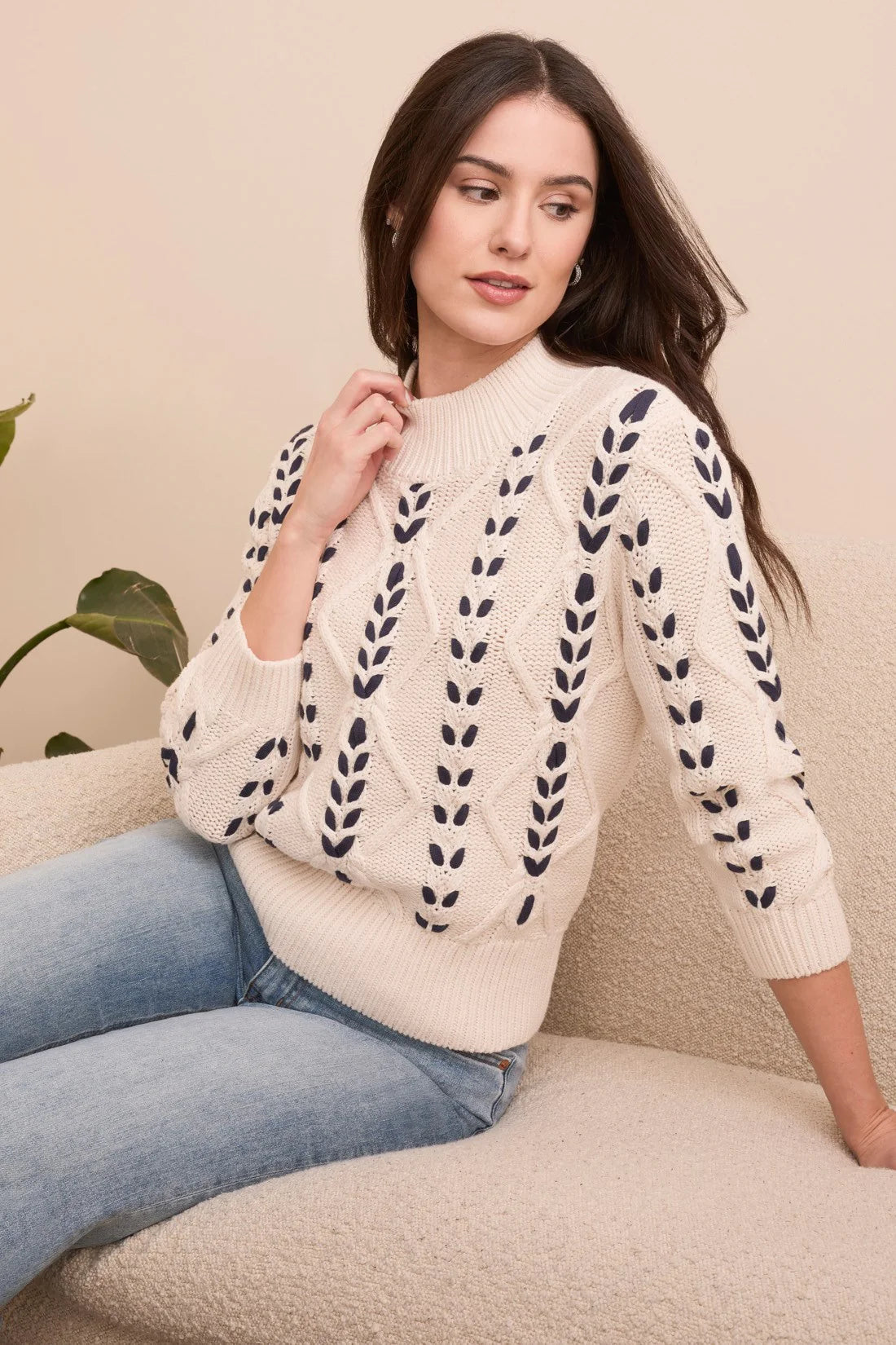 Woman wearing a cream sweater with black leaf patterns sitting on a beige couch.