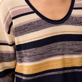 Close-up of a person wearing a knit sweater with horizontal stripes in navy, cream, beige, and mustard yellow.