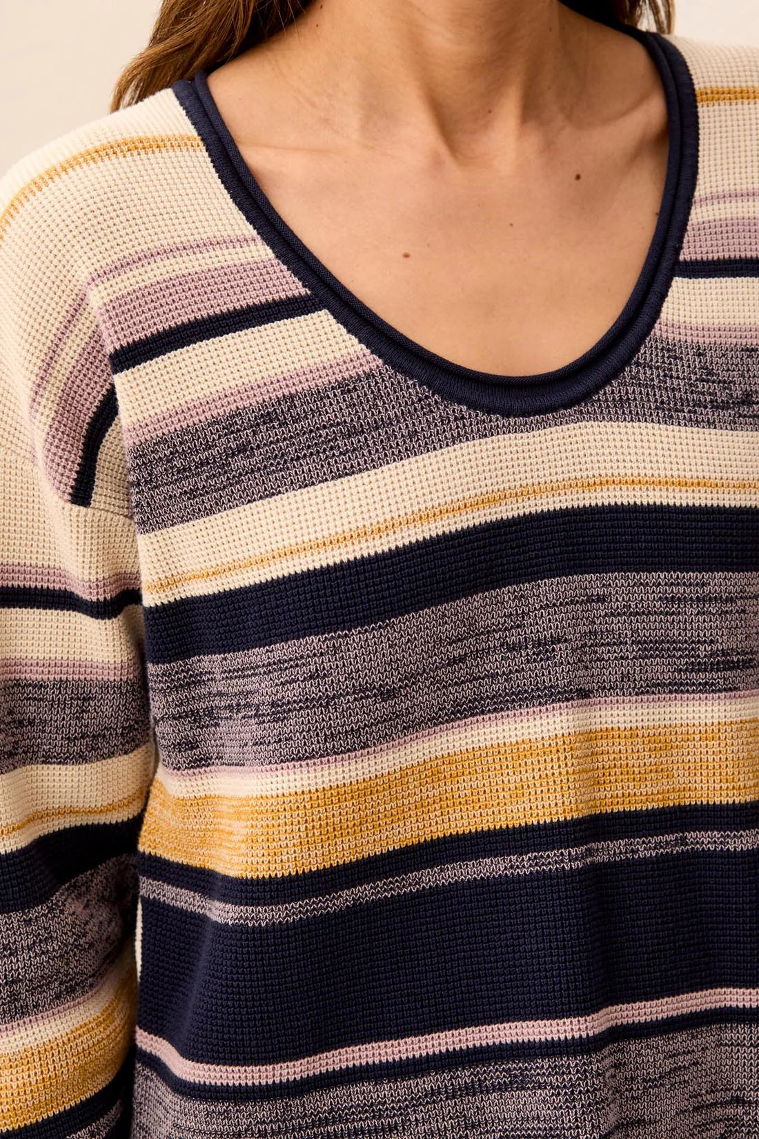 Close-up of a person wearing a knit sweater with horizontal stripes in navy, cream, beige, and mustard yellow.