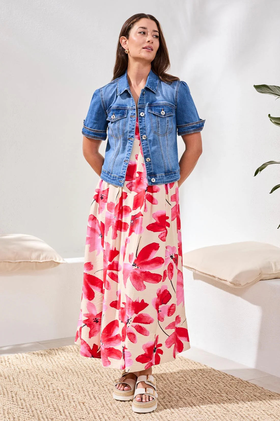 Woman wearing a floral dress with a denim jacket in a minimal indoor setting