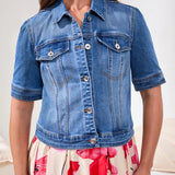 Woman wearing a blue denim jacket over a floral dress on a white background