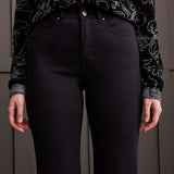 Person wearing black floral-patterned top and black pants against a neutral background