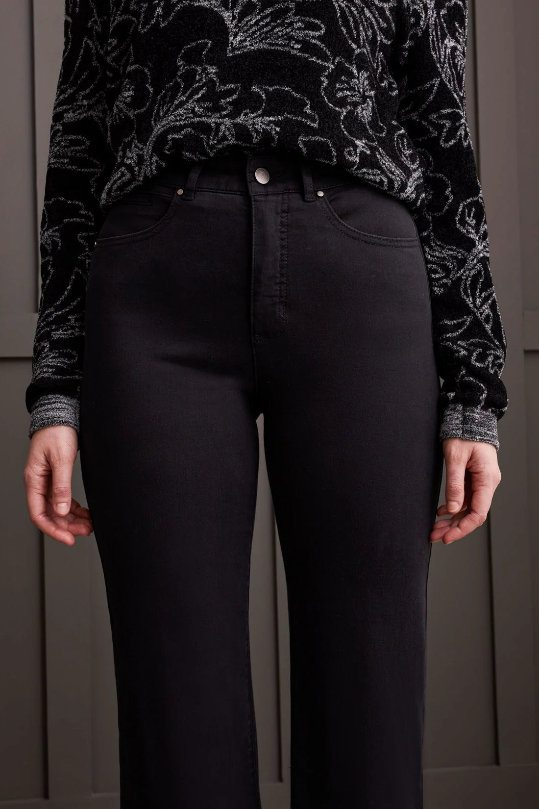 Person wearing black floral-patterned top and black pants against a neutral background
