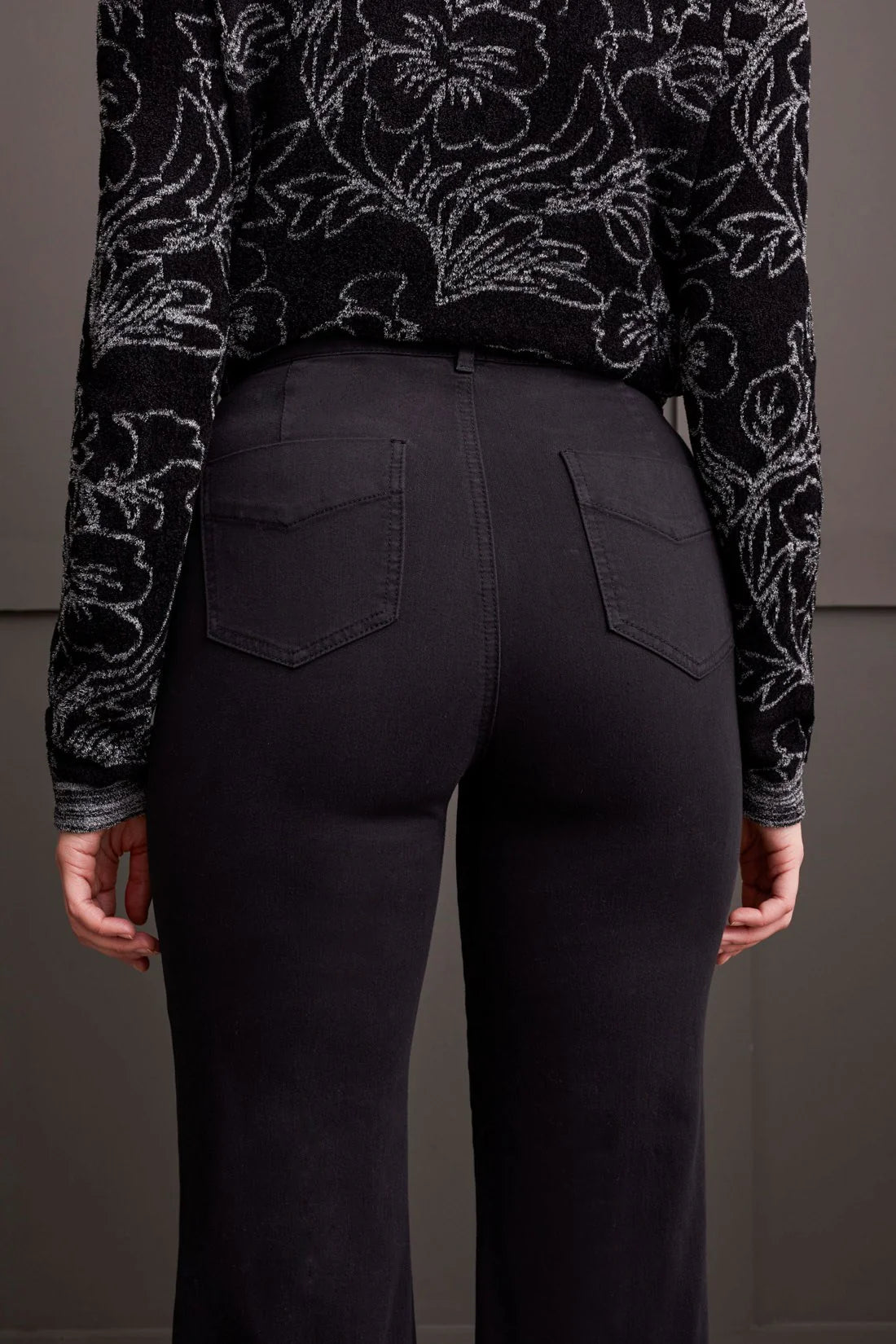 Person wearing black pants with a patterned top against a gray background