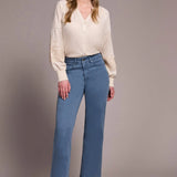 Woman wearing a cream blouse and blue jeans against a plain background