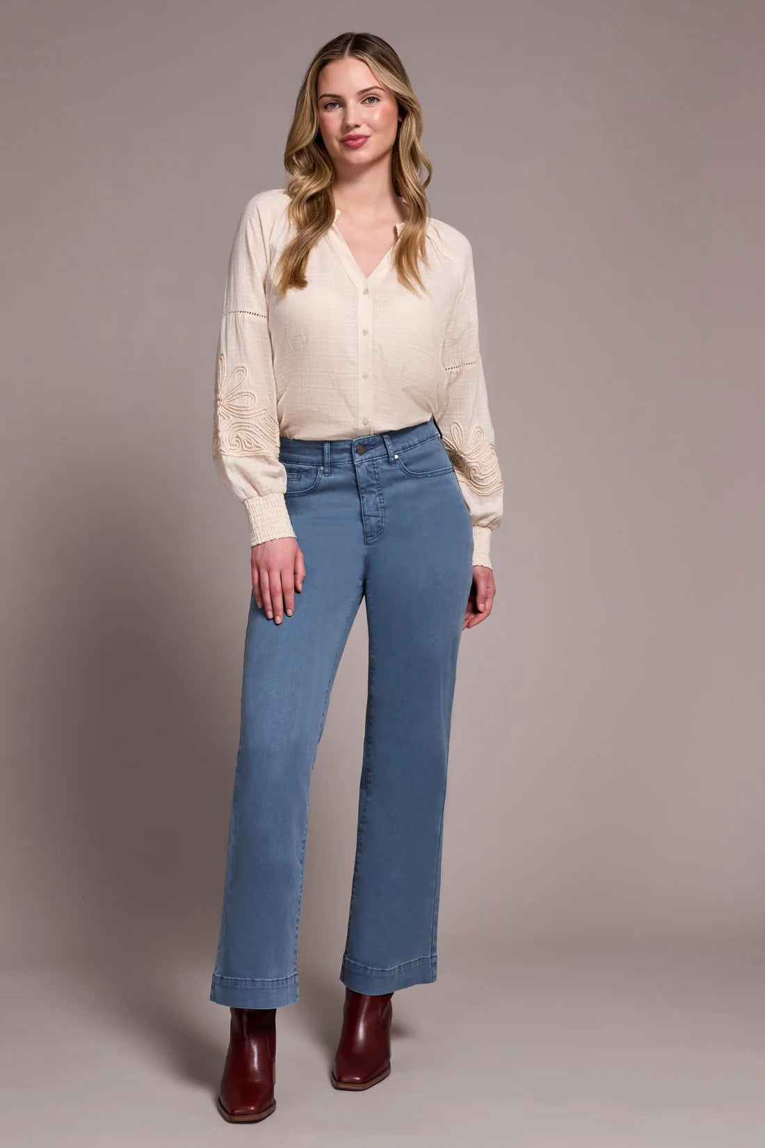 Woman wearing a cream blouse and blue jeans against a plain background