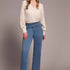 Woman wearing a cream blouse and blue jeans against a plain background