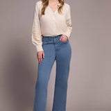 Woman wearing a cream blouse and blue jeans against a plain background