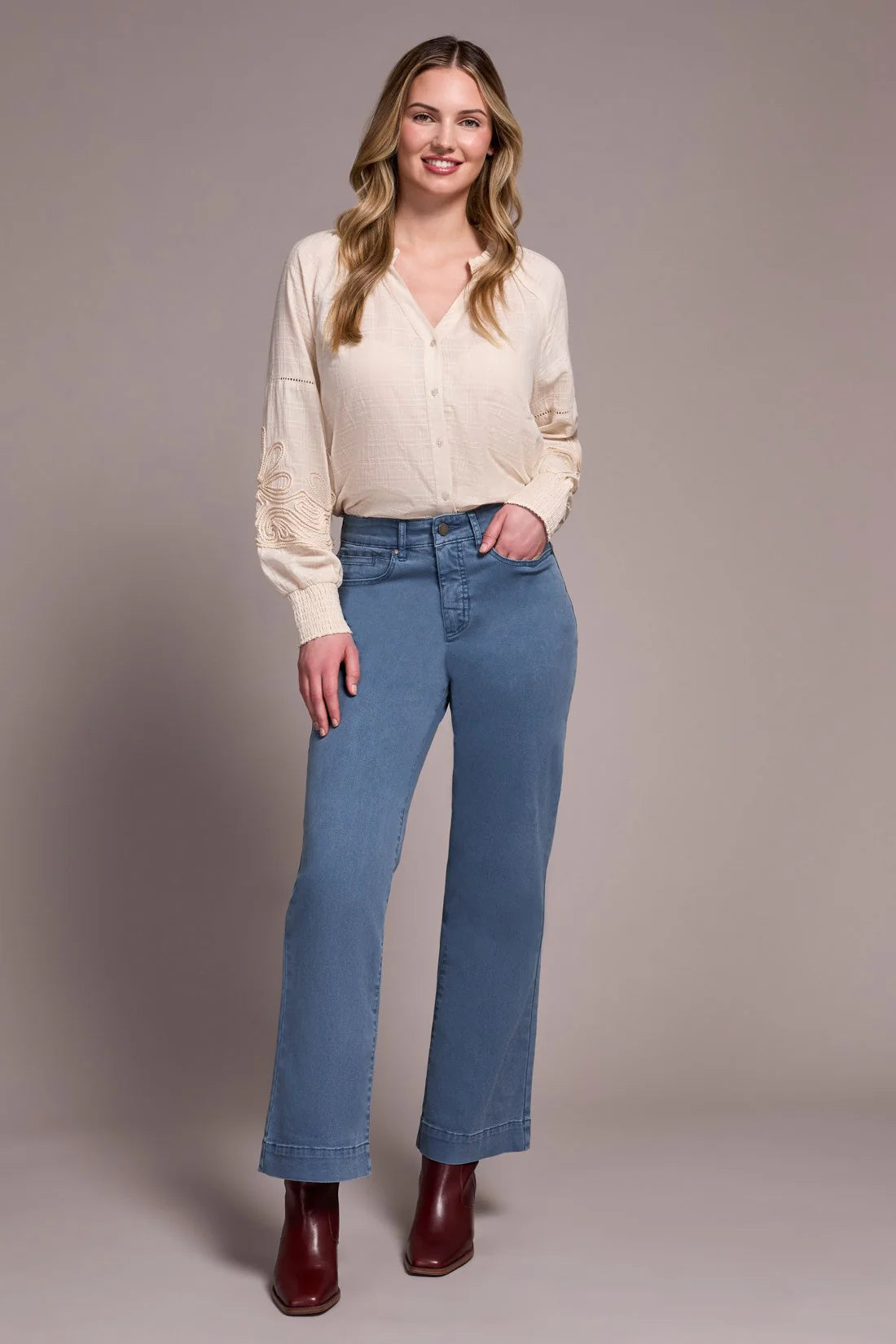 Woman wearing a cream blouse and blue jeans against a plain background