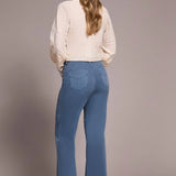Woman wearing blue jeans and a beige blouse against a plain background