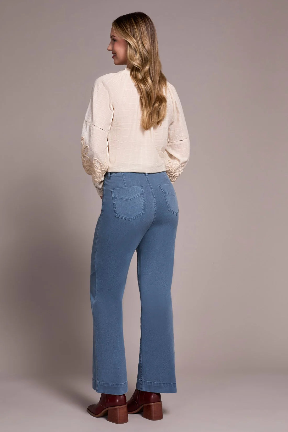 Woman wearing blue jeans and a beige blouse against a plain background