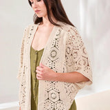Woman wearing a beige crochet cardigan over a green jumpsuit against a white background