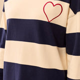 A close-up of a person wearing a long-sleeve crewneck sweatshirt with horizontal navy blue and cream stripes, featuring a red outline heart embroidered on the chest.