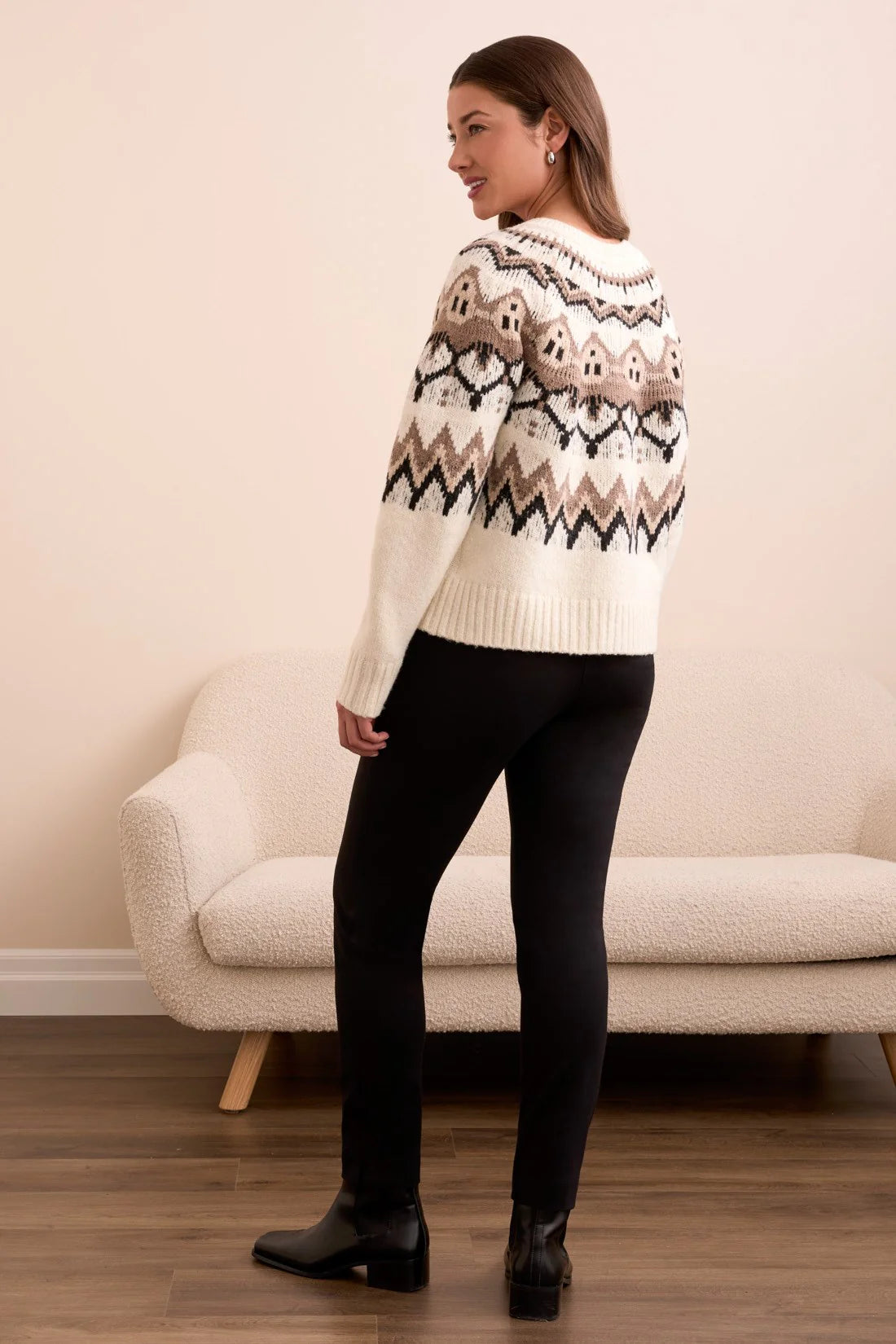 Woman wearing a patterned sweater standing in a room with a beige sofa.