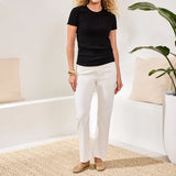 Woman wearing a black t-shirt and white pants standing in a room with a plant and cushions.