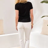 Woman wearing a black t-shirt and white pants in a minimalistic room.
