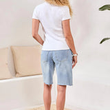 Woman wearing a white t-shirt and light blue shorts in a room with beige cushions and a plant.