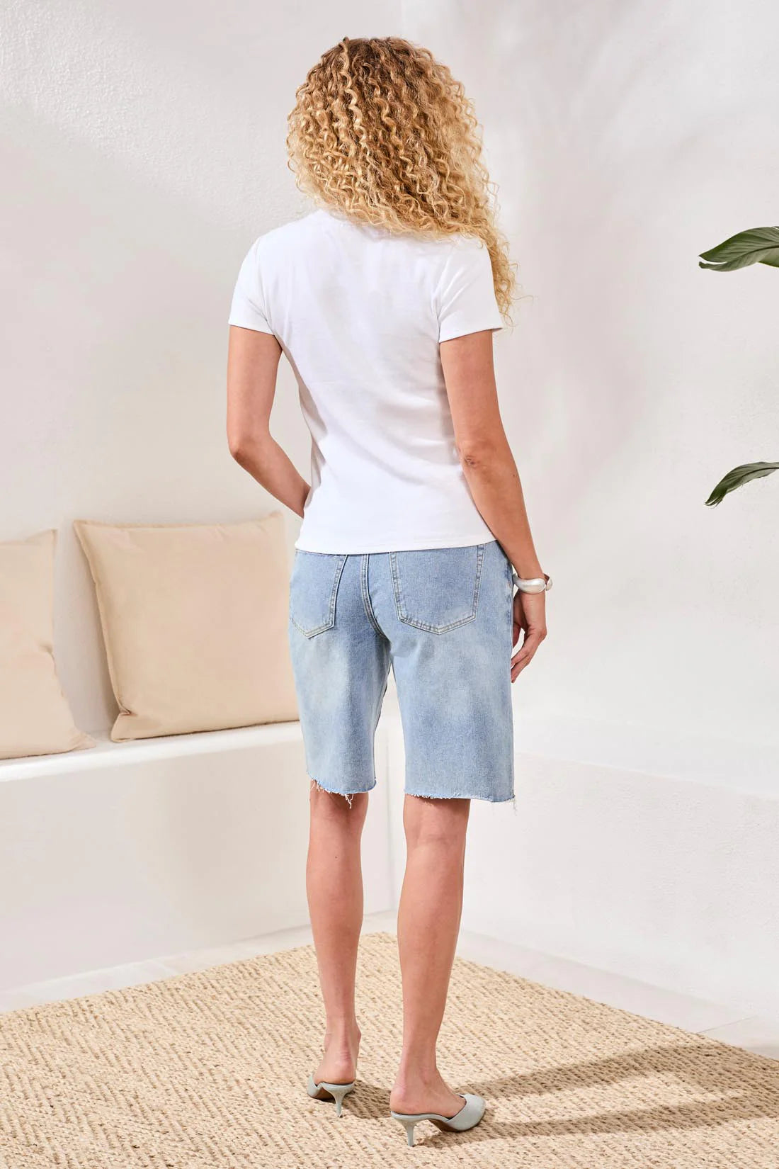 Woman wearing a white t-shirt and light blue shorts in a room with beige cushions and a plant.