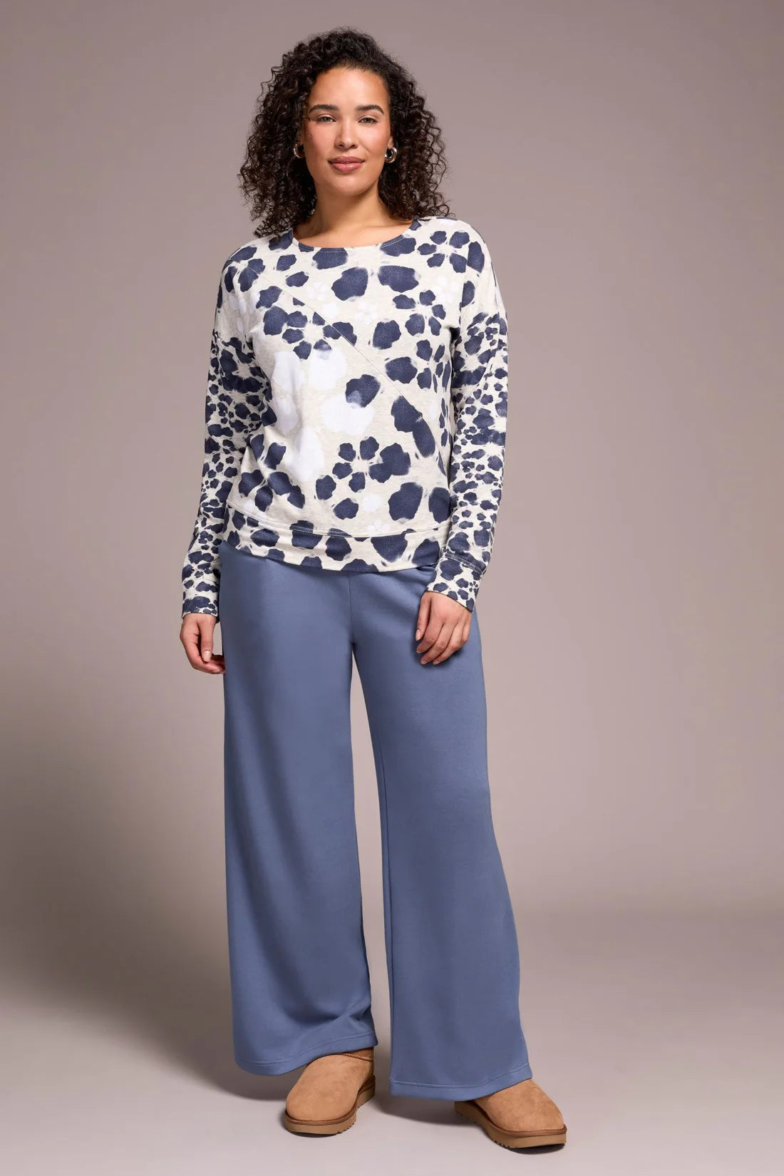 Woman wearing a patterned top and blue pants against a plain background