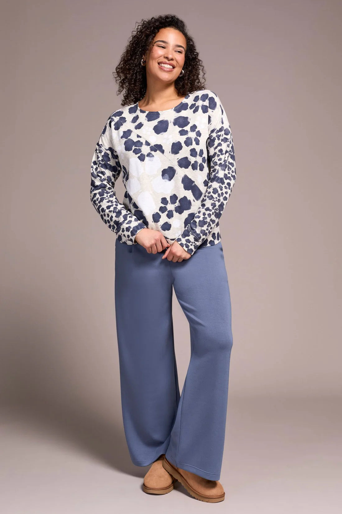 Woman wearing a patterned top and blue pants against a plain background