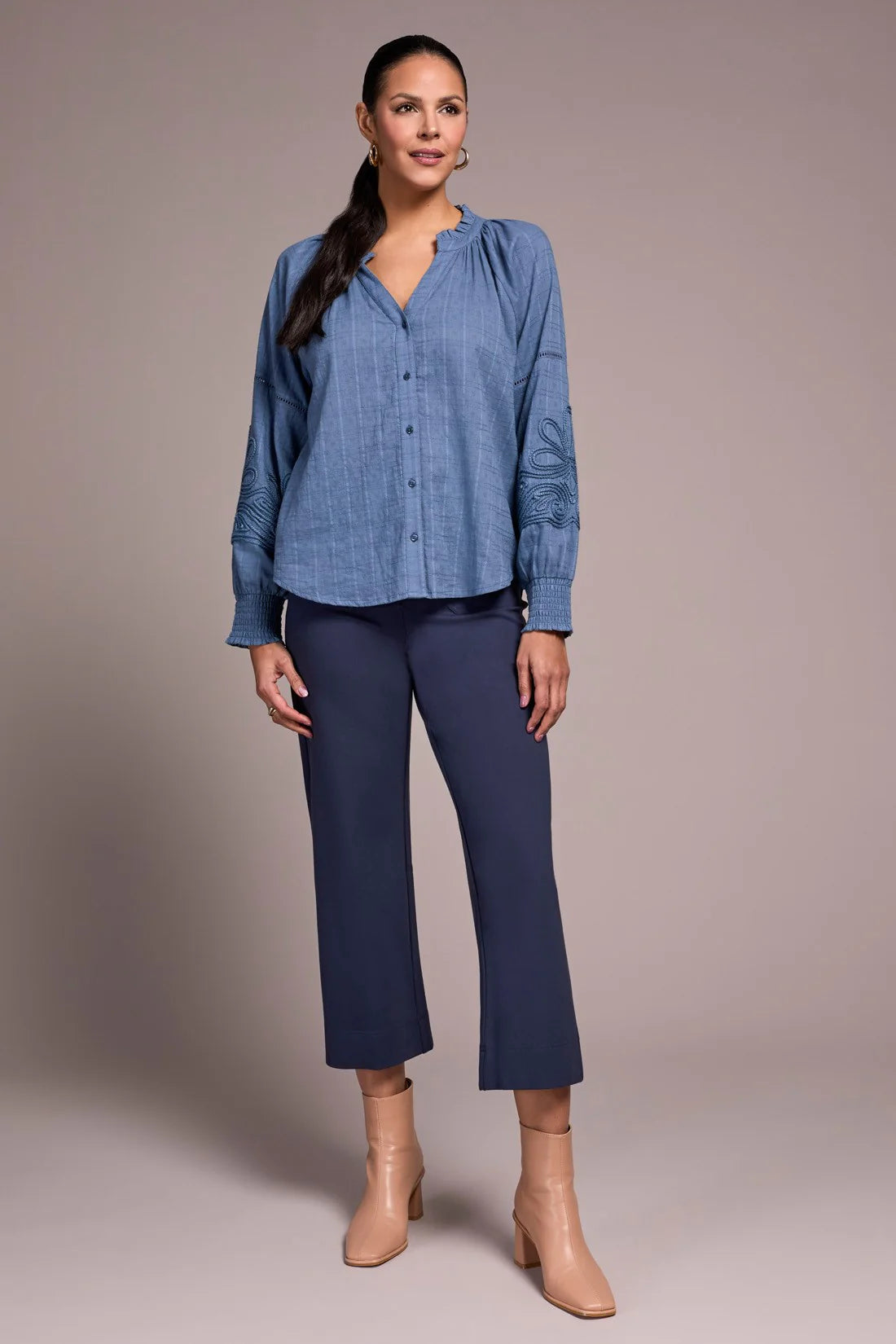 Woman wearing a blue blouse and navy pants against a plain background