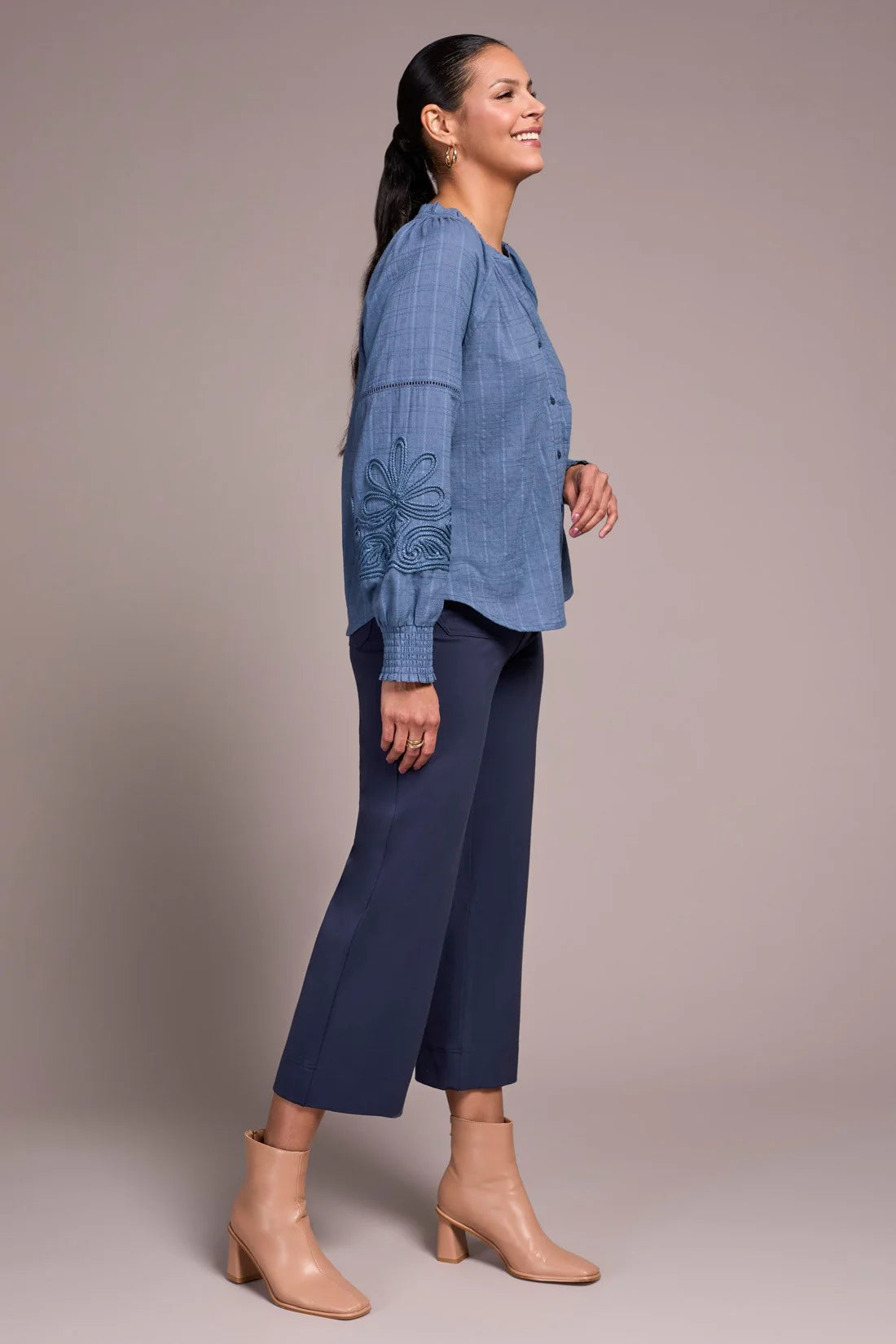 Woman wearing a blue shirt and navy pants against a plain background
