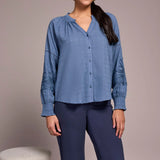 Woman wearing a blue shirt and dark pants standing against a plain background