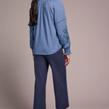 Woman wearing a blue embroidered blouse and pants on a plain background